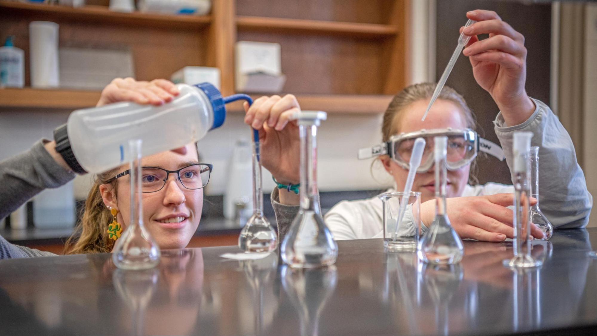 Two students dropping chemicals into glass beakers.